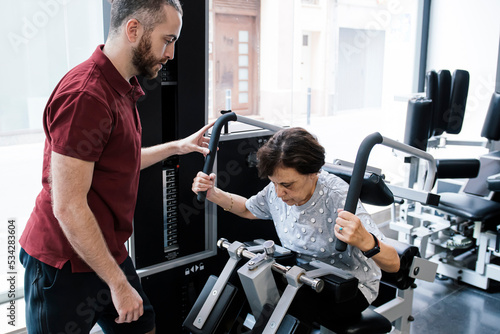 Older woman working out on the machines at the gym with her personal trainer