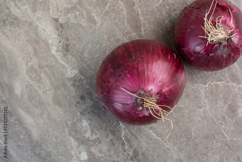 Two whole red onion bulbs on marble background