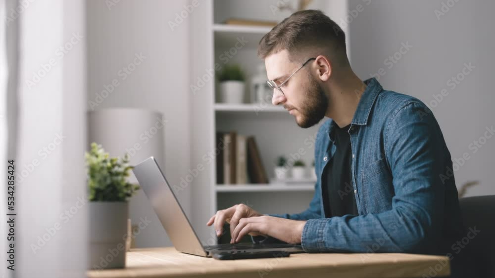 Handsome bearded man typing on laptop, young coder writing code, home office light interior Handsome bearded man typing on laptop, young coder writing code, home office light interior