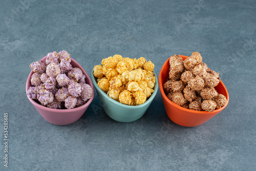 A colorfully assorted variety of popcorn candy flavors assorted in small bowls on marble background