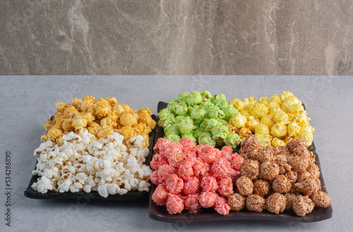 Three plates of various colored popcorn candies and simple popcorn on marble background