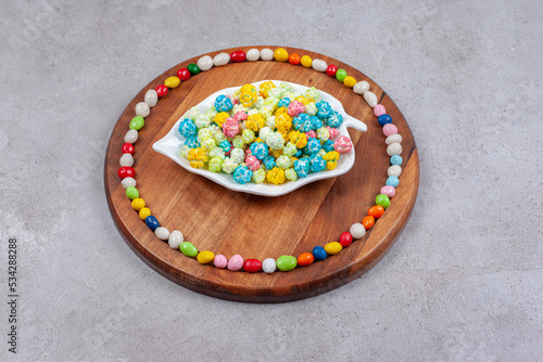 Candies on and around an ornate platter on wooden board, on marble background