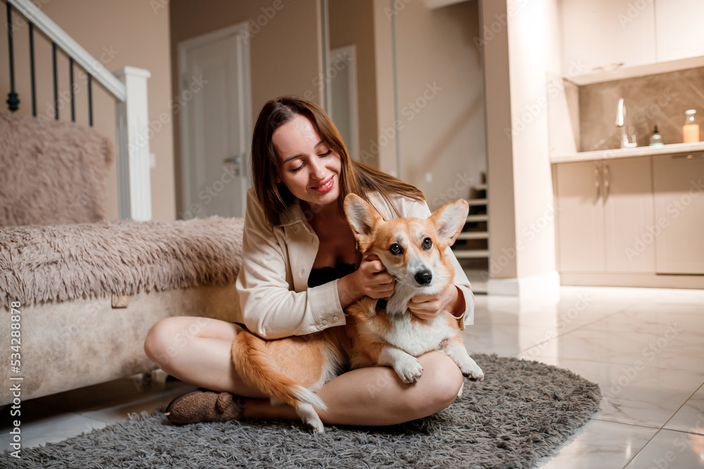 Attractive girl hug and play with corgi dog at home. Welsh Corgi Pembroke with his owner woman on the floor at living room Attractive girl hug and play with corgi dog at home. Welsh Corgi Pembroke with his owner woman on the floor at living room