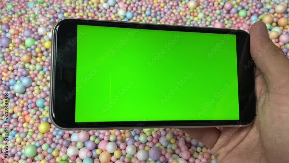 Chroma key green screen on smartphone landscape in male hand with colourful pastel rainbow foam ball beads in background Chroma key green screen on smartphone landscape in male hand with colourful pastel rainbow foam ball beads in background