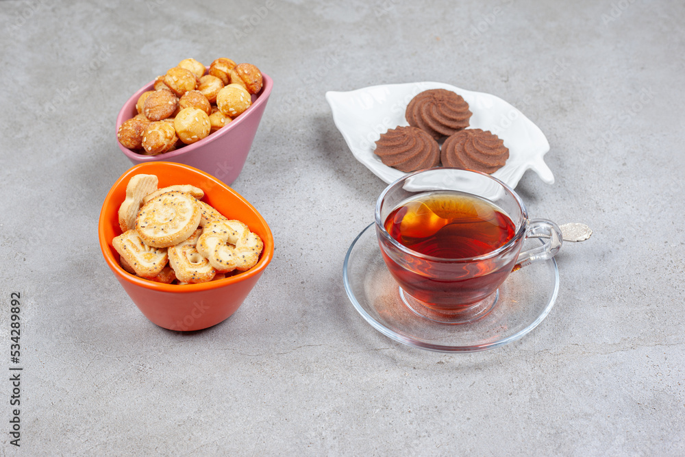 A plate of cookies, two bowls of cookie chips and a cup of tea arranged on marble background A plate of cookies, two bowls of cookie chips and a cup of tea arranged on marble background