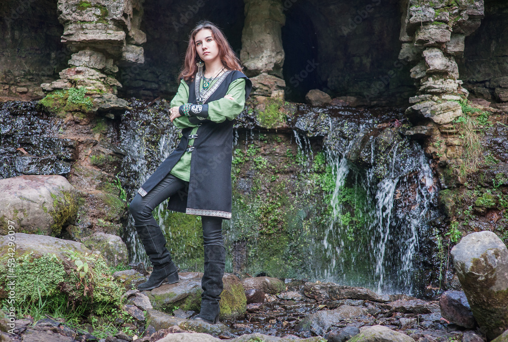 Young beautiful woman wearing man’s medieval style dress standing near waterfall Young beautiful woman wearing man’s medieval style dress standing near waterfall