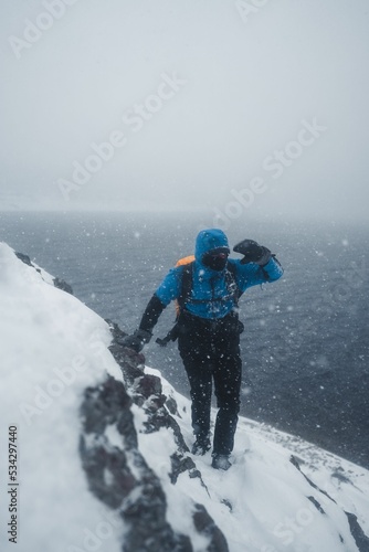 Canvas Print Mesmerizing vertical view of snowy stormy hillside at the ocean with a hiker - g