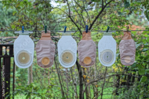 a row of brown white plastic medical colostomy bags hang on a wire on the street among green vegetation photo