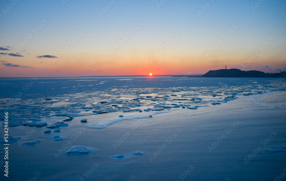 Aerial view of sunset over the frozen sea. Winter landscape on seashore during dusk. View from above of melting ice in ocean on sunrise with horizon. Global warming. Vivid colorful skyline scenics.