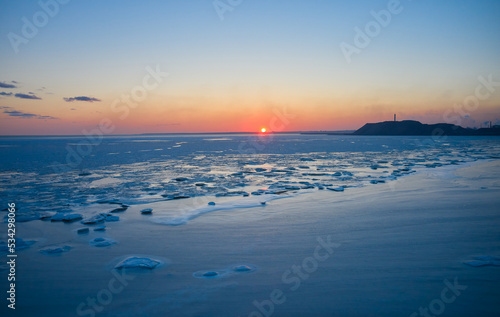 Aerial view of sunset over the frozen sea. Winter landscape on seashore during dusk. View from above of melting ice in ocean on sunrise with horizon. Global warming. Vivid colorful skyline scenics.