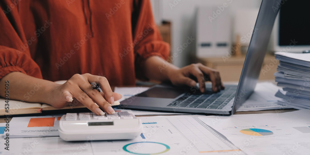 Business woman using calculator and laptop for do math finance on wooden desk in office and business working background, tax, accounting, statistics and analytic research concept Business woman using calculator and laptop for do math finance on wooden desk in office and business working background, tax, accounting, statistics and analytic research concept