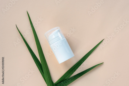 White cosmetic bottle and green leaves on beige background. Top view  flat lay  mockup