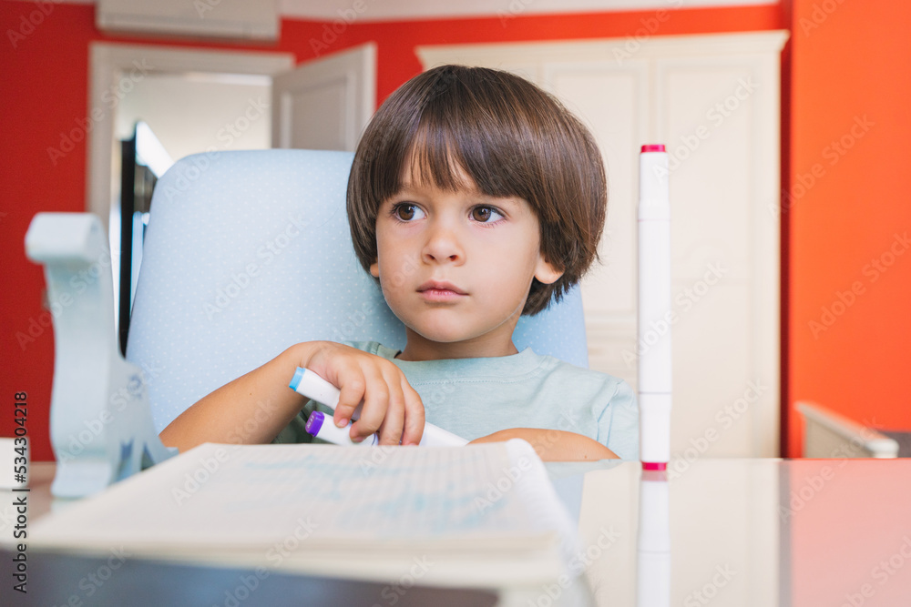 Smart kid with a notebook studying online at his colorful room remotly during pandemic Smart kid with a notebook studying online at his colorful room remotly during pandemic