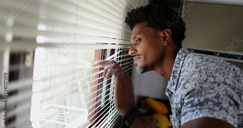 Принти на полотні Black man looking through kitchen blinders looking outside