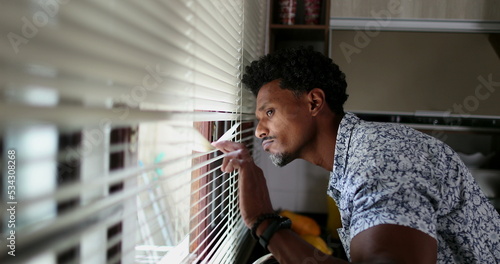 Black man looking through kitchen blinders looking outside