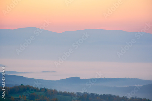 foggy autumn morning. beautiful landscape in mountains at sunrise. forested hills and glowing mist in the distance valley © Pellinni