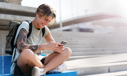 Young woman with a backpack using her mobile phone while sitting on the sidewalk. photo