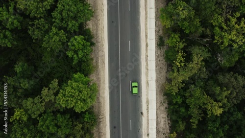 Cinematic aerial top down view of the green car on the road between green forest. Drone slow motion shot of the road in the forest.