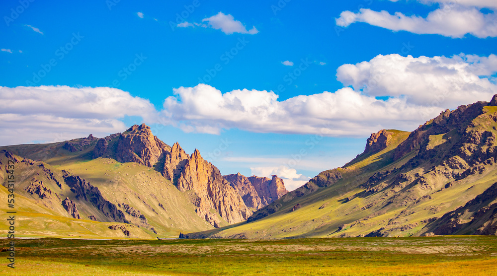 Beautiful nature of the rocky mountains. Mountain nature landscape. Rocks on the background of the sky with clouds. Mountain valley with green hills.