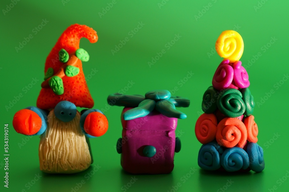 Fototapeta premium A toy gnome with a Christmas tree and a gift on a green background. New Year and Christmas. Fabulous scenery.