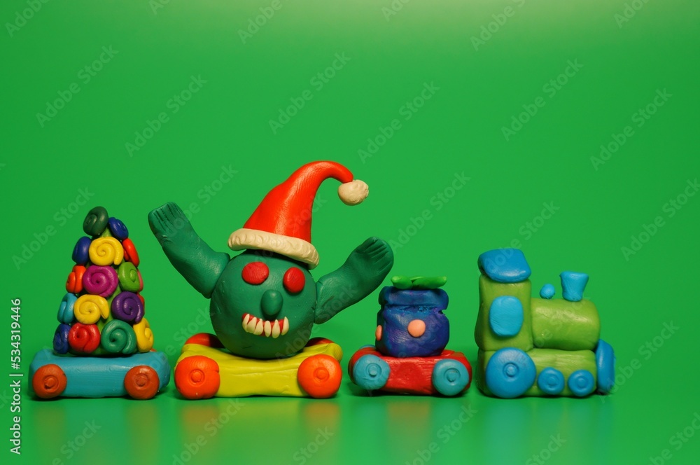 Obraz premium A toy train with a Christmas tree, a gift and a figure of a virus in a festive hat. Christmas toys. A festive event. New Year and Christmas. Green background.