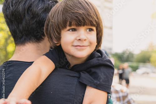 Little boy on his father shoulder looking away coming from a playground with a beautiful brown hair and eyes