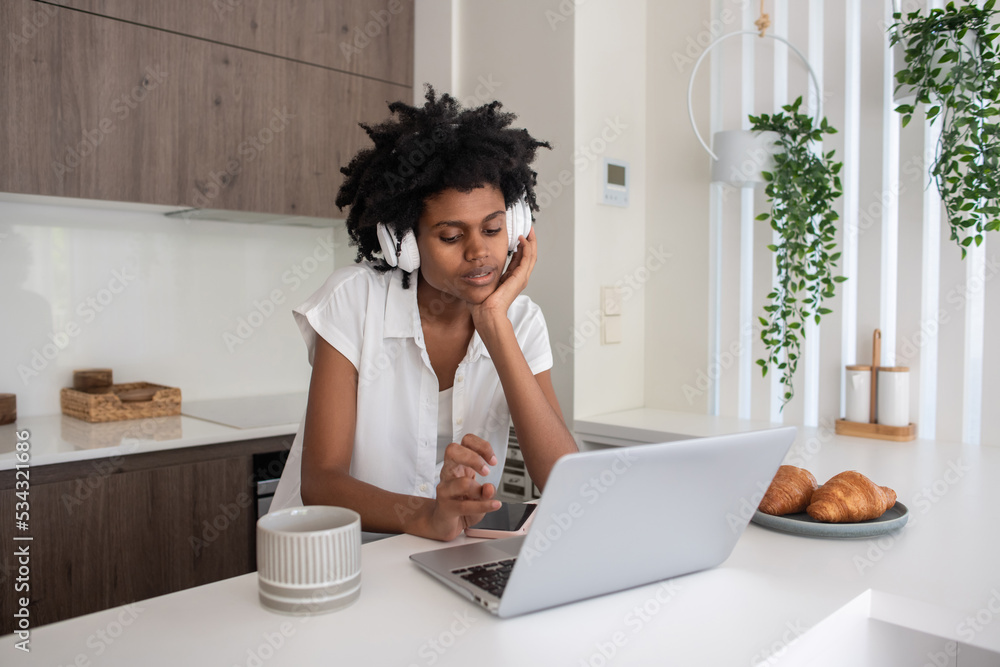 Woman in headphones working from home during pandemic. African American businesswoman sitting at desk, working on laptop during lockdown. Home office, epidemic, business, quarantine concept Woman in headphones working from home during pandemic. African American businesswoman sitting at desk, working on laptop during lockdown. Home office, epidemic, business, quarantine concept
