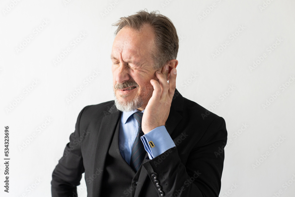 Portrait of mature businessman suffering from otitis. Senior Caucasian manager wearing formal suit frowning from ear pain against white background. Earache concept Portrait of mature businessman suffering from otitis. Senior Caucasian manager wearing formal suit frowning from ear pain against white background. Earache concept