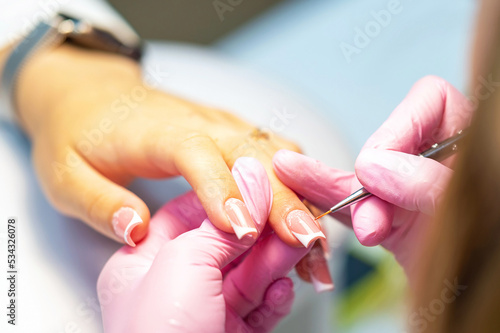 Nail design for a young girl or woman is drawn by a manicure master, a manicurist with a brush in a beauty salon. Nail care during manicure procedure.