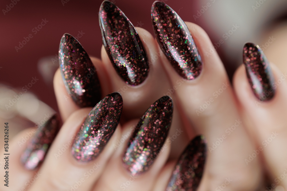 Woman hand with long nails and a bottle of dark red burgundy nail