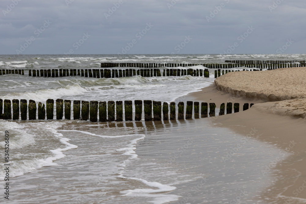 Seaside landscape, foamy water of the Baltic Sea with a wooden breakwater. Cloudy sky, Island Wolin, Miedzyzdroje, Poland