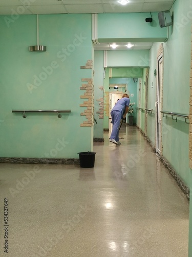 A woman in a medical uniform is mopping the floors in the hospital corridor.