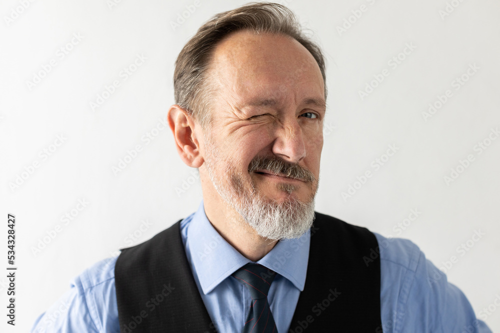 Close-up of positive mature businessman blinking eye against white background. Portrait of bearded senior Caucasian manager wearing formalwear looking at camera and smiling. Flirt or hint concept Close-up of positive mature businessman blinking eye against white background. Portrait of bearded senior Caucasian manager wearing formalwear looking at camera and smiling. Flirt or hint concept