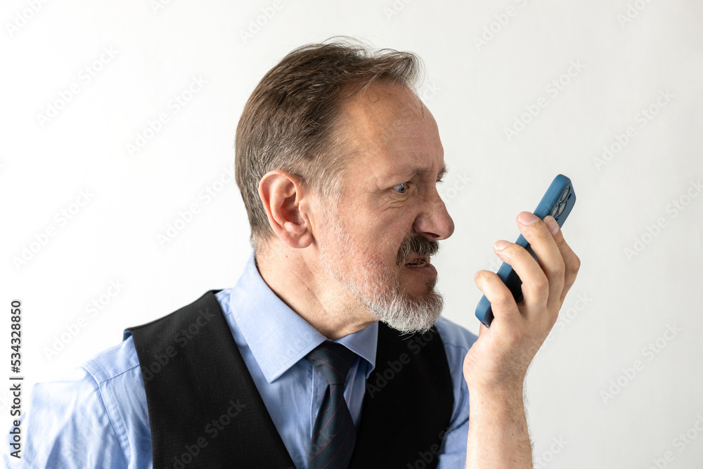 Portrait of angry mature businessman recording audio message. Senior Caucasian manager wearing formalwear answering to client with irritation. Unpleasant conversation concept Portrait of angry mature businessman recording audio message. Senior Caucasian manager wearing formalwear answering to client with irritation. Unpleasant conversation concept