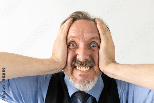 Close-up of excited or frustrated mature businessman. Senior Caucasian manager wearing formalwear staring, clenching teeth and holding head in hands against white background. Shock or awe concept