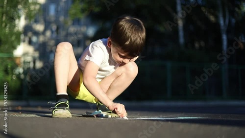 The boy draws with crayons on the asphalt . Children 's drawings . Outdoor games.