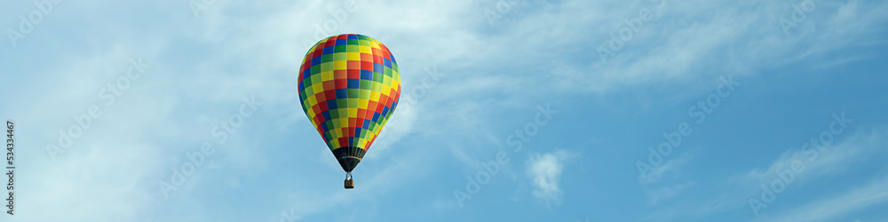 Naklejka premium 4x1 banner with a flying multi-color balloon against the background of a blue sky with clouds