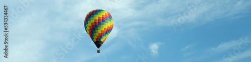 4x1 banner with a flying multi-color balloon against the background of a blue sky with clouds