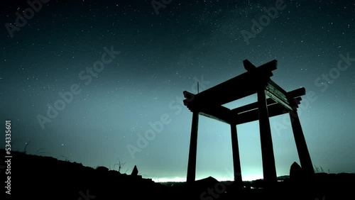 the dark silhouette of asian building on top of hill over  citylights on the backgriund of night sky with moving stars