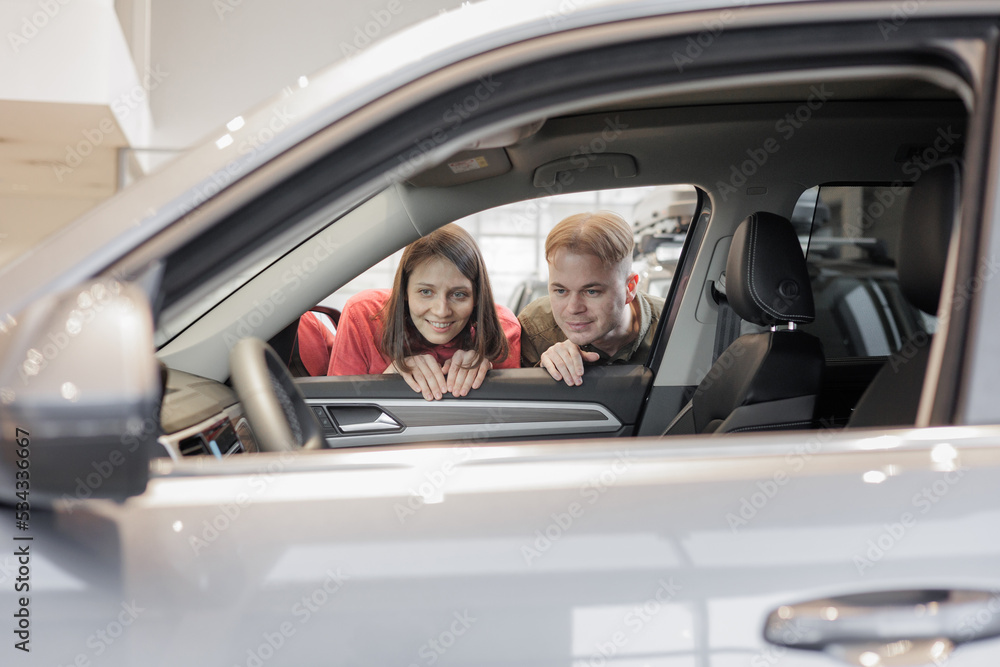 man and a woman couple in a car dealership buy or trade in. car rental or repair service. happy and successful married couple choose a new car on credit. happy two people holding keys and laughing man and a woman couple in a car dealership buy or trade in. car rental or repair service. happy and successful married couple choose a new car on credit. happy two people holding keys and laughing