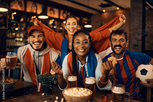 Happy soccer fans cheering while watching game on TV in pub. © Drazen