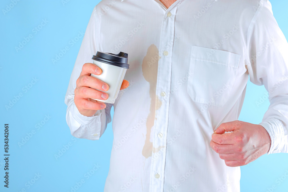 A man showing a dirty coffee stain on shirt a blue background. Spoiled clothes. Dirty coffee stain on clothes. daily life stain concept A man showing a dirty coffee stain on shirt a blue background. Spoiled clothes. Dirty coffee stain on clothes. daily life stain concept