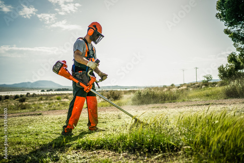 Backlit side view of a man removing grass with a trimmer photo