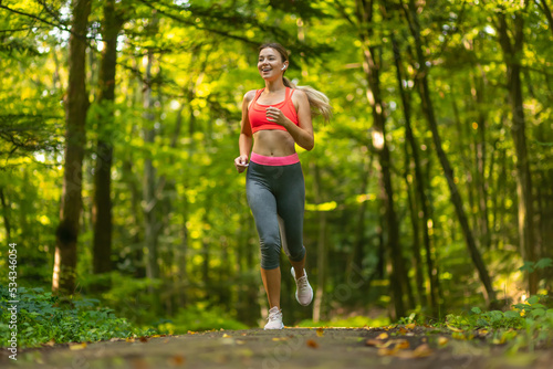 Happy woman running in city park. Girl runner jogging smiling aspirational outside on beautiful summer day.