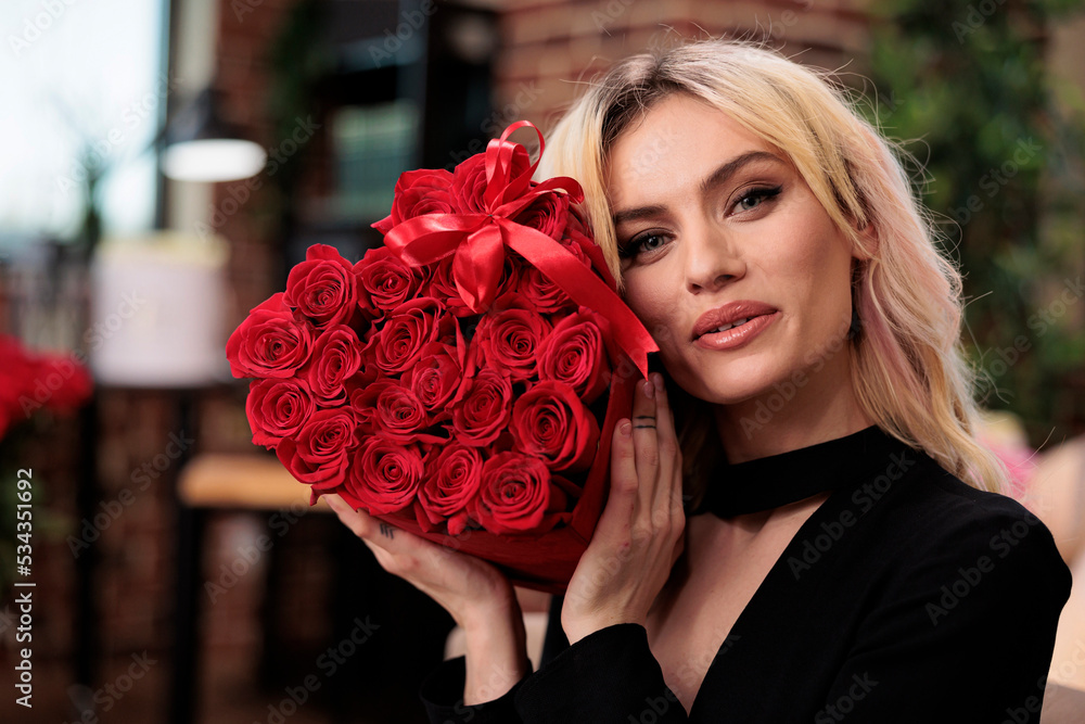 Beautiful woman holding luxury red roses looking at camera, valentines day gift. Attractive blonde girlfriend with flower bouquet in heart shaped box portrait, romance holiday celebration фотография Stock