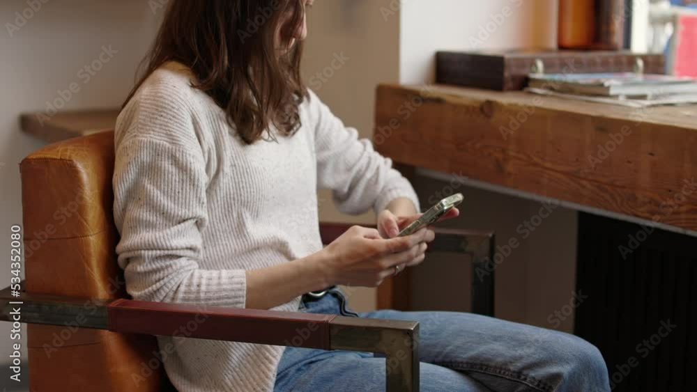 Unrecognizable business woman sitting in armchair at wooden desk and typing on cellphone answering email in coffeeshop during break with free wifi 4k Unrecognizable business woman sitting in armchair at wooden desk and typing on cellphone answering email in coffeeshop during break with free wifi 4k
