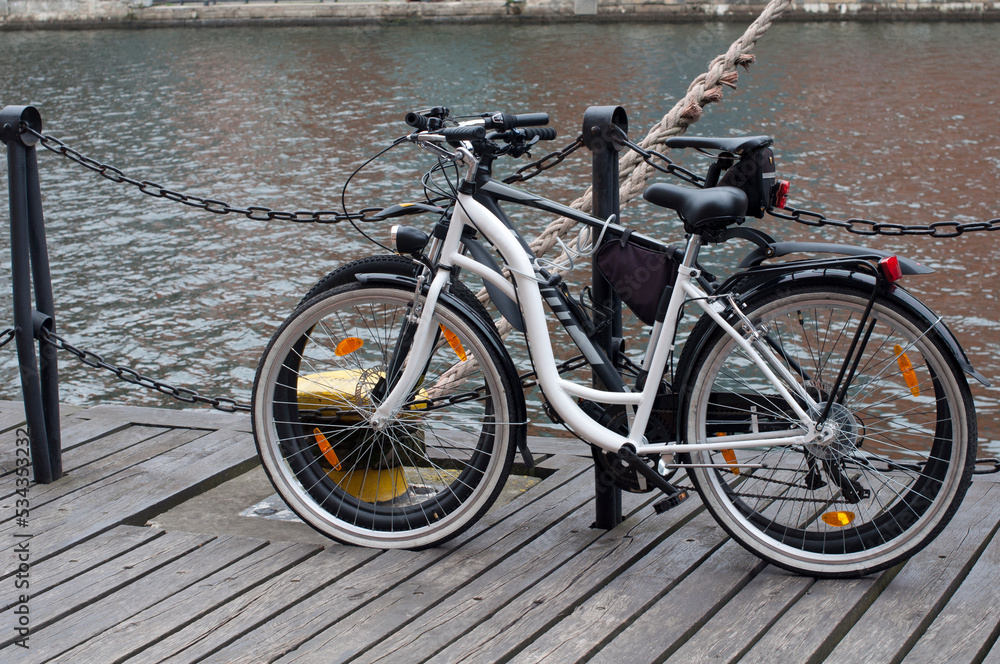 Two bicycles are parked near the water canal. White and black bicycles on the Gdansk embankment