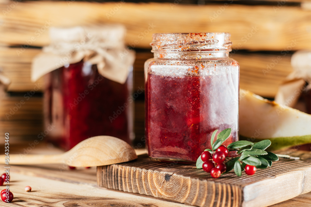 Φωτογραφία Jars of homemade lingonberry and pear jam with craft paper on lids on wooden surface next to fresh lingonberries and pears
