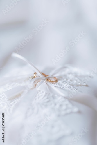 Photography Vertical shot of gold wedding rings on a white lacy ring bearer pillow