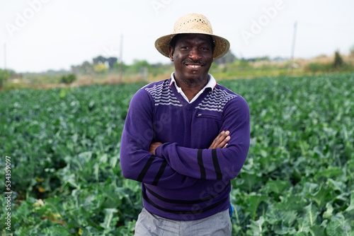 Young adult confident man farm worker standing on field with growing broccoli at sustainable farm
